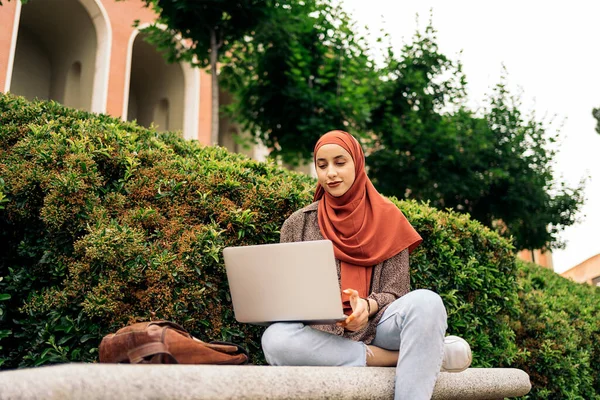 公園に座って 彼女のコンピュータを使用して頭のスカーフを身に着けている美しい若い女性 — ストック写真