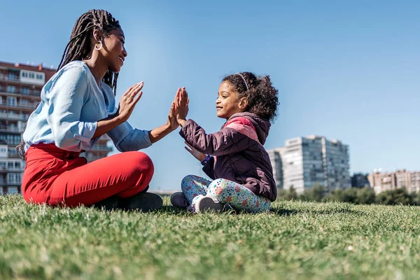 Adorável Afro Menina Sentado Grama Com Sua Mãe Divertindo Durante — Fotografia de Stock