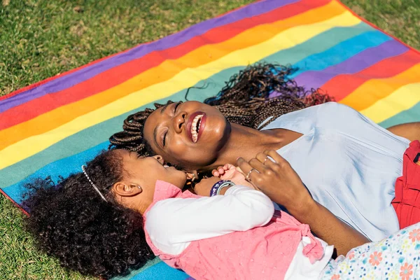 かわいいですアフロ女の子横たわっでザ草でカラフルなピクニック毛布で彼女のお母さんと楽しい晴れた日 — ストック写真