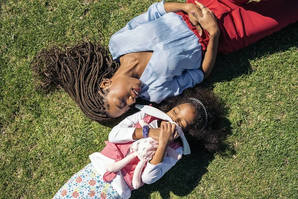 草の中に若い娘の隣に寝そべって笑っている黒人女性 — ストック写真