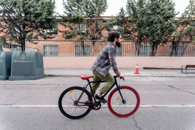 Hippi sakallı adam sokakta bisiklete biniyor ve önüne bakıyor..