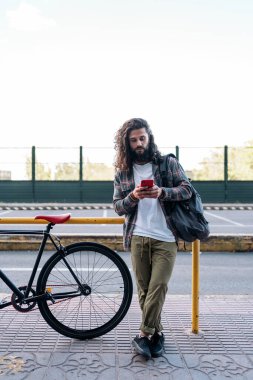 Şehirde bisikletinin yanında duran ve cep telefonunu kullanan sakallı havalı bir adam..