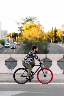 Havalı hippi sakallı adam şehirde bisikletini sürüyor ve önüne bakıyor..