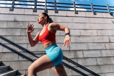 Güneşli bir günde şehirde spor kıyafetleriyle spor yapan güçlü Asyalı kadın. Merdivenlere tırmanıyor..