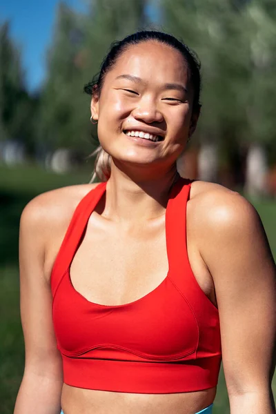 Active asian woman with sports clothes working out in the park during sunny day. She is smiling and looking at camera.