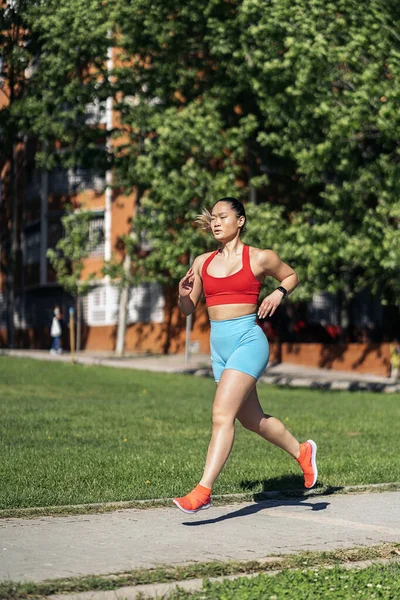 晴れた日に公園でスポーツウェアが働いている強力なアジアの女性 彼女は走って正面を見ている — ストック写真