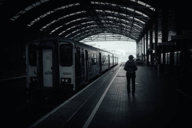 Tren istasyonunda yalnız bir insanın dramatik siyah beyaz görüntüsü.