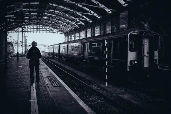 Tren istasyonunda yalnız bir insanın dramatik siyah beyaz görüntüsü.