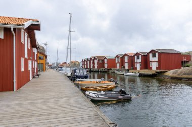 Smogen, İsveç - 9 Haziran 2021: Kanalın her iki tarafında yelkenli ve balıkçı kulübeleri bulunan su kanalı boyunca yürüyen ahşap köprü