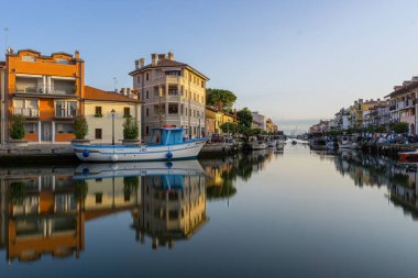 Grado, İtalya - 8 Temmuz 2021: Turist kasabası Grado 'da sabahın altın saatinde sular üzerindeki binalar ve yansımalarla