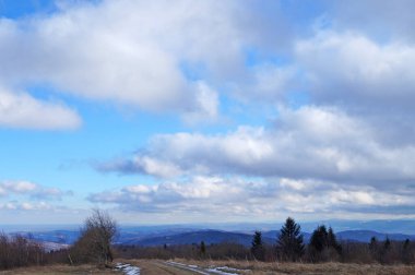 Gri bulutlu mavi gökyüzünün altında ormanla kaplı sonbahar dağlarının manzarası