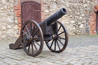 Güneşli bir günde, yüksek bir kale taşından duvarın yanında tekerlekler üzerinde eski demir top.