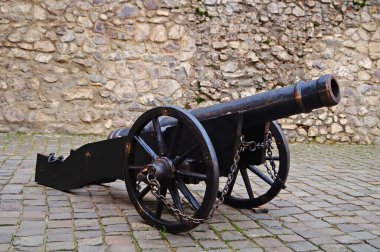 Güneşli bir günde, yüksek bir kale taşından duvarın yanında tekerlekler üzerinde eski demir top.