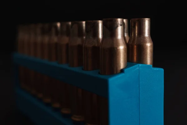 Amber gold empty bullet cases in blue holder aginst a dark black background with copy space available