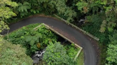 drone video view of the jungle in the beautiful mountains in Indonesia, it appears motorized vehicles pass through the highway through the forest.