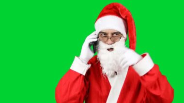 Noel Baba, yeşil arka planda izole edilmiş bir şekilde cep telefonuyla konuşuyor. Noel bir tatil konseptidir. Aile tatili. 