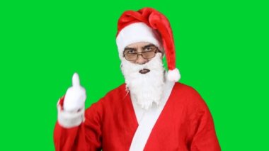 Noel Baba 'nın portresi kameraya bakıyor ve başparmağını kaldırıp göz kırpıyor. Yeşil arkaplanda izole. 