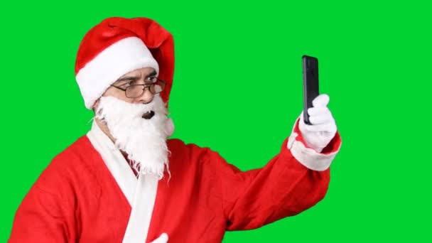 形象圣诞老人站在那里 用智能手机展示自己的大拇指 与绿色背景隔离 — 图库视频影像