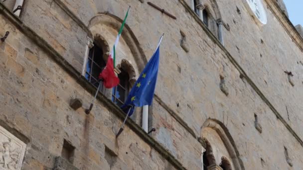 イタリアと欧州連合 の旗の詳細は イタリアのトスカーナ州のVolterra町の歴史的中心部にある古代のパラッツォ プリオリのファサードにかかっています — ストック動画