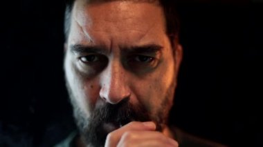 Karanlık bir odada sakallı duman bulutu üfleyerek nefes alan bir adamın portresi. Siyah arkaplanda yüzünüzü kapatın. Yavaş çekim