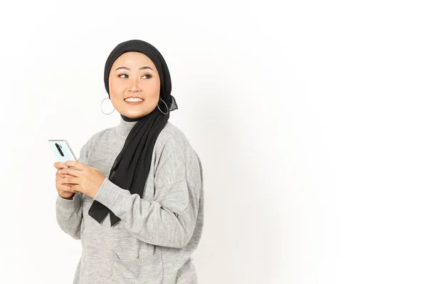 笑顔と白い背景に隔離されたヒジャブを身に着けている美しいアジアの女性のスマートフォンを使用して — ストック写真