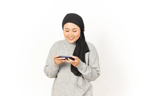 白い背景に隔離されたヒジャブを身に着けている美しいアジアの女性のスマートフォンでモバイルゲームをプレイ — ストック写真