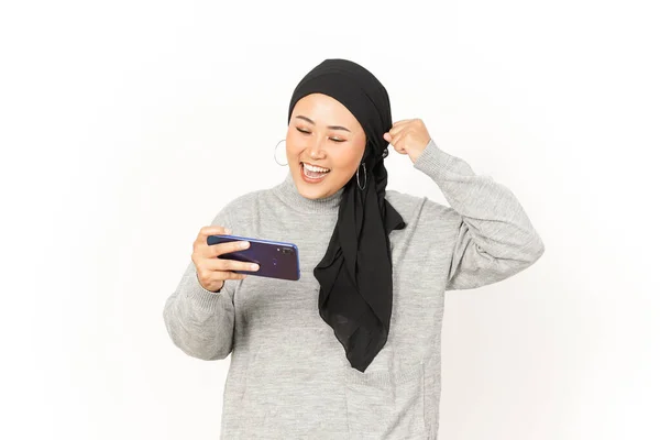 白い背景に隔離されたヒジャブを身に着けている美しいアジアの女性のスマートフォンでモバイルゲームをプレイ — ストック写真