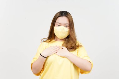 Wearing Mask and Hands on Chest of Beautiful Asian Woman wearing yellow T-Shirt Isolated On White