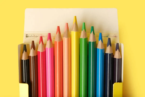 Multicolored pencils in a box isolated on yellow.