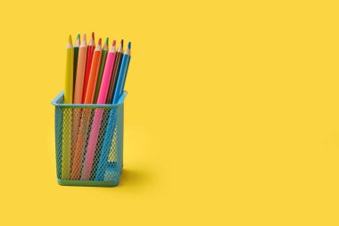 Sarı arkaplanda izole edilmiş mavi bir klasördeki çok renkli kalemler..