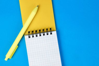 Notepad and yellow pen on a blue background. Minimalism, top view, space for text