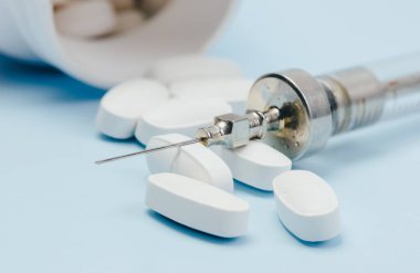 Old-fashioned vintage syringe on a background of scattered pills on a blue background. Close-up, macro. Medical concept.