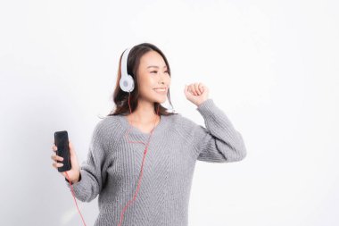 Gri kazak giyen genç güzel bir kadın yalan söylüyor ve beyaz arka planda izole edilmiş beyaz kulaklıklar takarak müzik dinliyor. Rahatlatıcı ve mutlu.