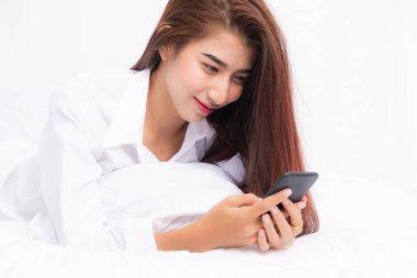 Genç Asyalı kadın yatak odasında akıllı telefon kullanıyor. Mutlu ve gülümsüyor..