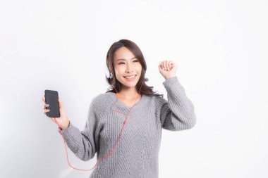 Gri kazak giyen genç güzel bir kadın yalan söylüyor ve beyaz arka planda izole edilmiş beyaz kulaklıklar takarak müzik dinliyor. Rahatlatıcı ve mutlu.