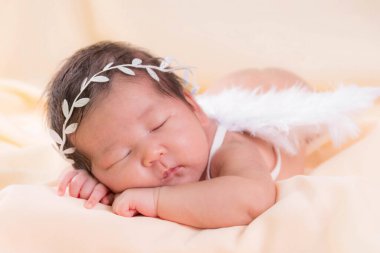 Bir aylık bir bebeğin portresi uyuyor, yeni doğmuş bir kız bebek. Beyaz bir saç bandı takıyor, melek kanatları takıyor ve krem rengi bir battaniyenin üzerinde uyuyor. Yeni doğan stüdyonun konsept portresi.