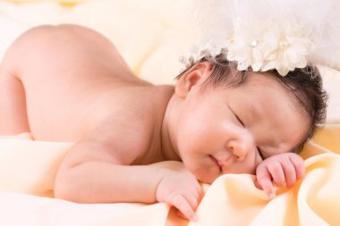 Bir aylık bir bebeğin portresi uyuyor, yeni doğmuş bir kız bebek. Çiçekli bir taç takıyor ve krem rengi bir battaniyenin üzerinde uyuyor. Yeni doğan stüdyonun konsept portresi.