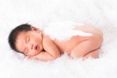 Bir aylık bir bebeğin portresi uyuyor, yeni doğmuş bir kız bebek. Tüylü melek kanatları takıyor ve beyaz bir battaniyenin üzerinde uyuyor. Yeni doğan stüdyonun konsept portresi.