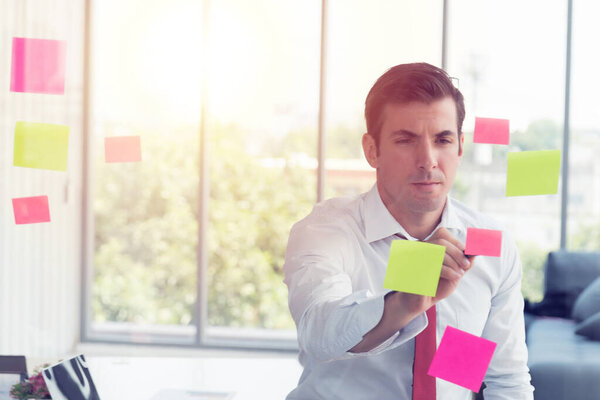 Businessman take notes at colorful chart on glass board is using the idea at his office, in the evening time.