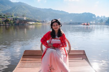 Tayland 'ın Mae Hong Son bölgesindeki Ban Rak Tayland köyünde ahşap bir teknede oturan kırmızı Hanfu antik Çin geleneksel elbisesi giyen çekici Asyalı kadın turist.