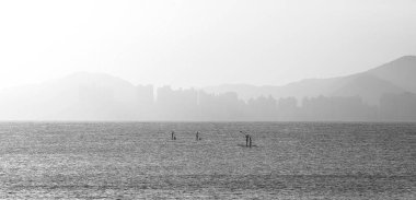 Gün batımında siyah beyaz fotoğraf çeken üç çift ayakta kürek çekiyor.