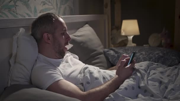 Giovane sdraiato nel letto con smartphone prima di dormire. — Video Stock