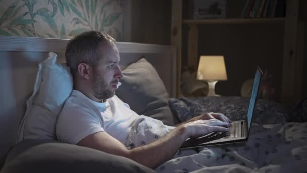 Ung man som ligger i sängen med laptop innan han sover — Stockvideo