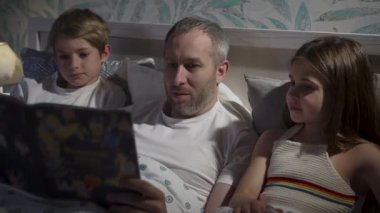 Yatakta dizüstü bilgisayar kullanan aile.