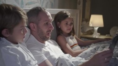 Yatakta dizüstü bilgisayar kullanan aile.