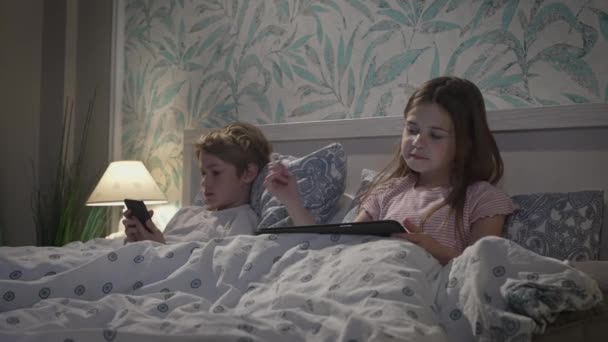 Bambini che utilizzano dispositivi digitali a letto — Video Stock