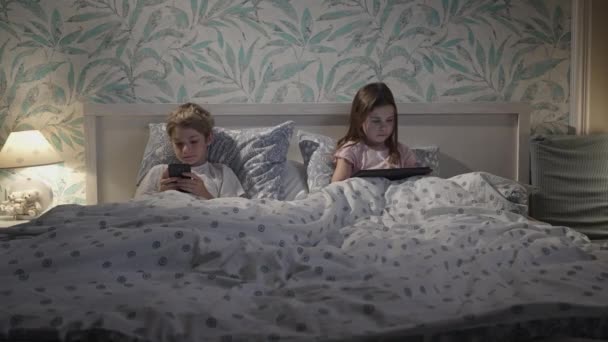 Niños usando dispositivos digitales en la cama — Vídeo de stock