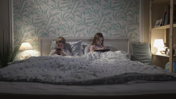 Niños usando dispositivos digitales en la cama — Vídeos de Stock