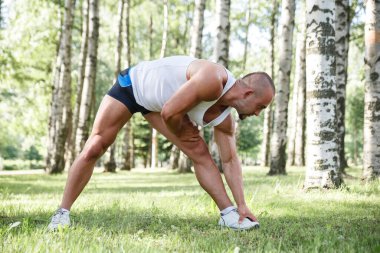 Genç atletik adam bir yaz günü huş ağaçlarının arasında spor için parka gider..