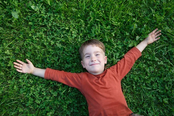 Mały Słodki Chłopiec Leży Zielonej Trawie Wyciągniętymi Ramionami Radośnie — Zdjęcie stockowe